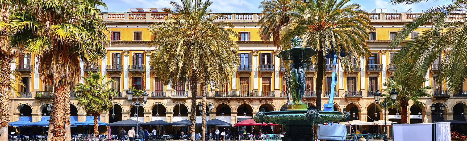 Royal area in Barcelona, Spain. Fountain with statues and high palm trees among traditional Spanish architecture at main central square of old town. Summer landscape with blue sky and clouds.